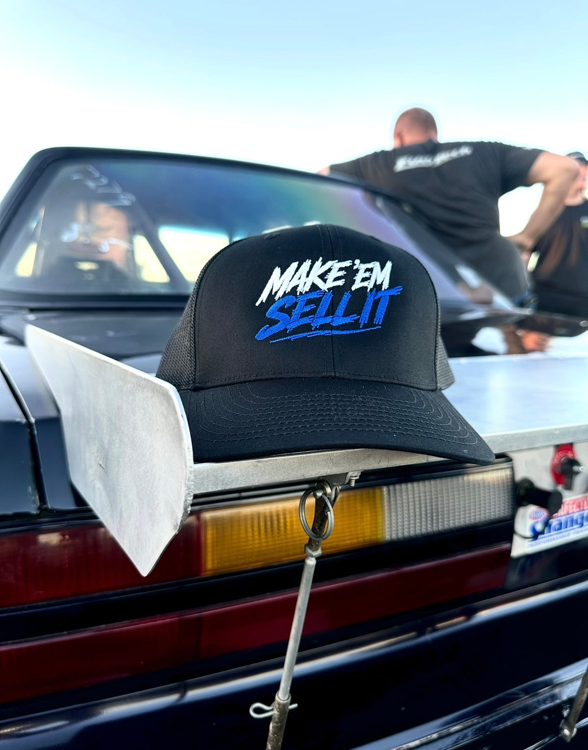 Make ’Em Sell It – Black Snapback Hat | White & Blue Embroidery